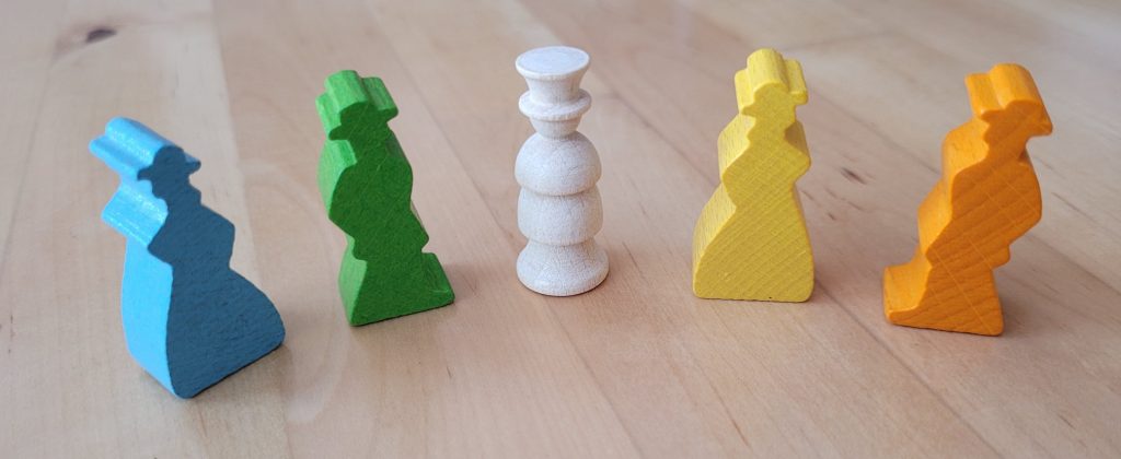 Fünf Spielfiguren von "Der Hexer von Salem" aus Holz. In Blau und Gelb die Silhouette von Frauen mit Hut und Kleidern. In Grün und Orange die von Männern mit Hut. In der Mitte der weiße Hexer mit Zylinder.