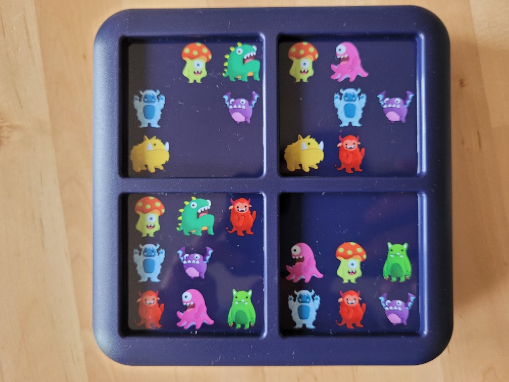 Der Spielplan ist eine in zwei mal zwei Felder eingeteilte Kunststoffbox, auf deren Felder verschiedene, bunte Monster zu sehen sind.