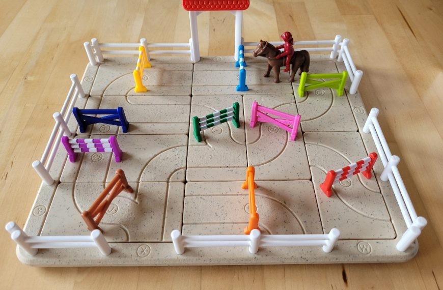 Der dreidimensionale Spielplan von "Schwing die Hufe" sieht aus wie ein Reitplatz mit einem Tor, Zaun und Reiter auf einem Pferd. Dazwischen stehen bunte Hindernisse.