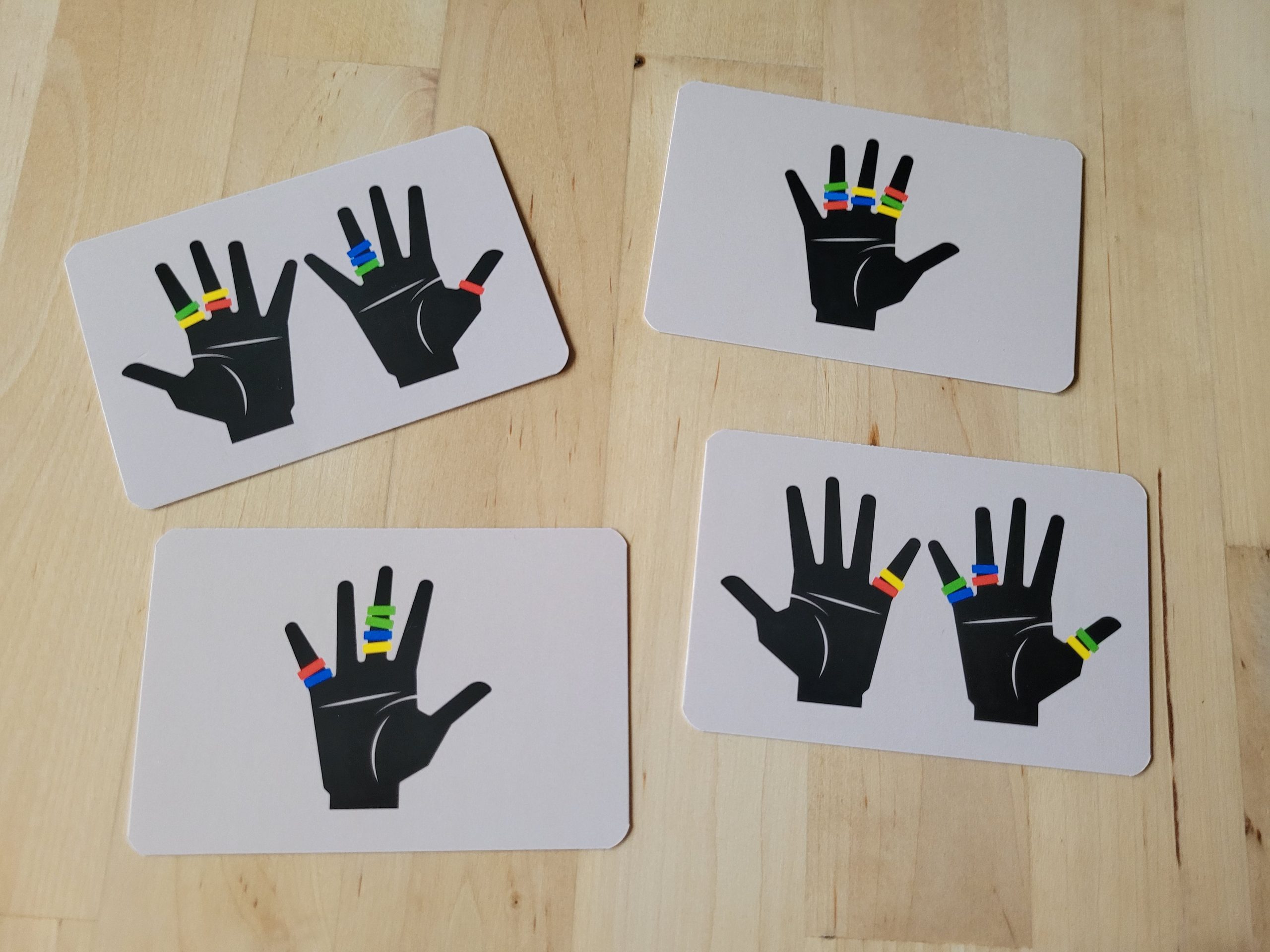 Vier Karten aus "Oh My Ring!" zeigen je zweimal eine und zweimal zwei Hände mit bunten Ringen.
