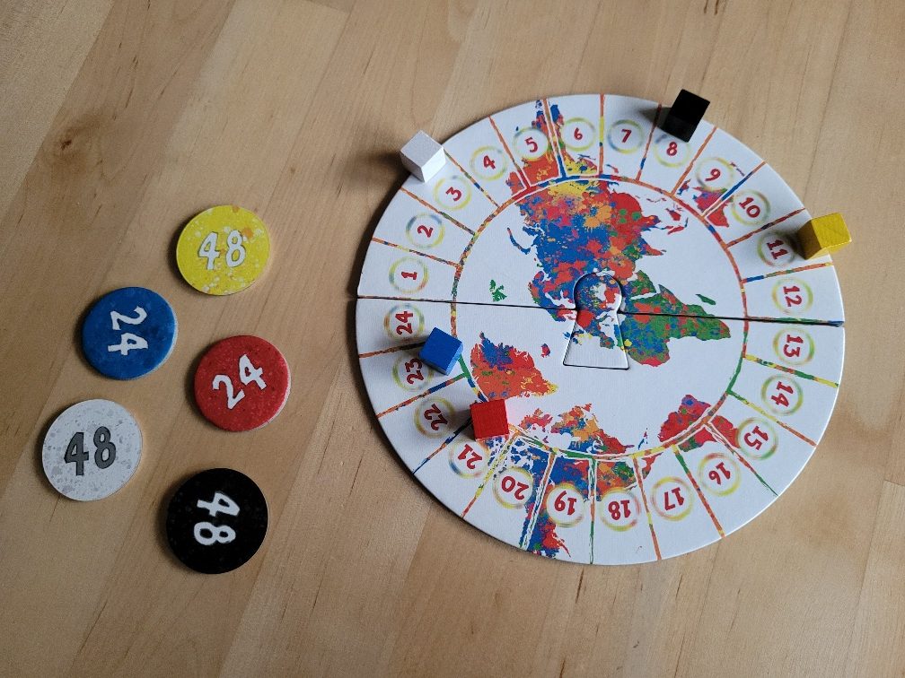 Der Spielplan ist ein Kreis mit einer bunten Weltkarte. Außen herum läuft eine Zahlreihe in Feldern von Eins bis 24. Darauf verteilt stehen fünf Spielfiguren. Daneben liegen fünf Zahlplättchen in Spielerfarben.