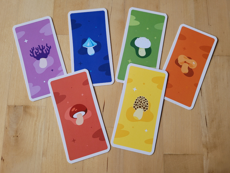Sechs Karten unterschiedlicher Farbe liegen auf einem Tisch. Sie geben bei "Kinoko" an, welche Pilze man sammelt.