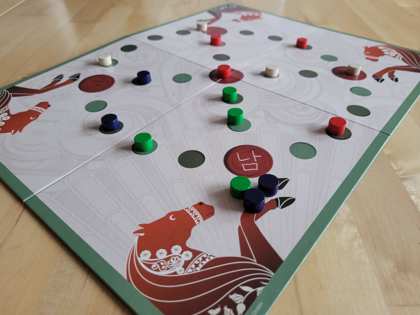 Der Spielplan von "Yut Nori" mit verschiedenfarbigen Spielsteinen. In den Ecken des Spielplans sind Pferde aufgedruckt.