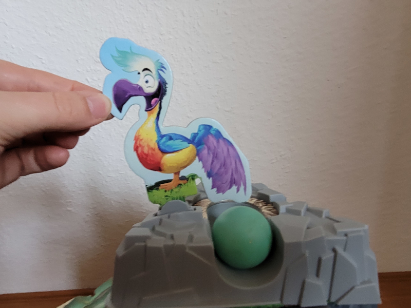 Eine Hand kippt einen Papp-Dodo und darunter kommt das Ei im Nest zum Vorschein.