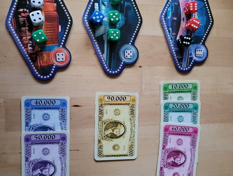 Auf drei Casino-Plättchen liegen unterschiedlich viele Würfel. Daneben liegen Gelscheine von 10.000 bis 90.000 Dollar.