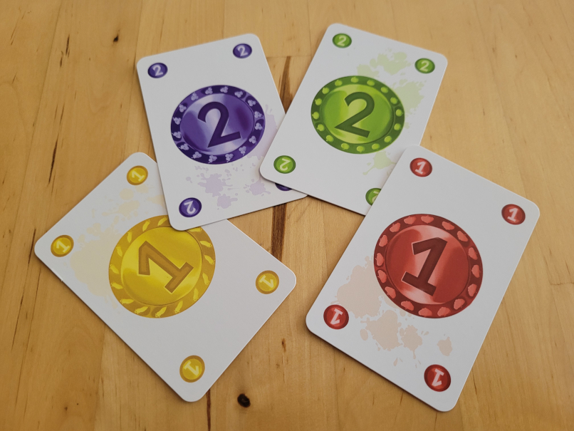 Vier Karten zeigen je zwei Münzen mit dem Wert eins und zwei. Die Münzen sind blau, gelb, grün und rot.