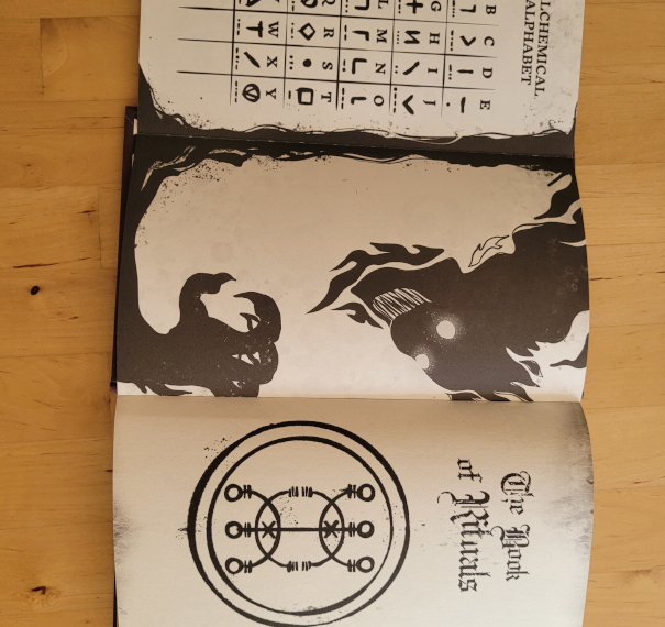 Buchseiten zeigen ein alchemistisches Alphabeth, eine schwarze, unheimliche Figur und den englischen Buchtitel "The Book of Rituals"