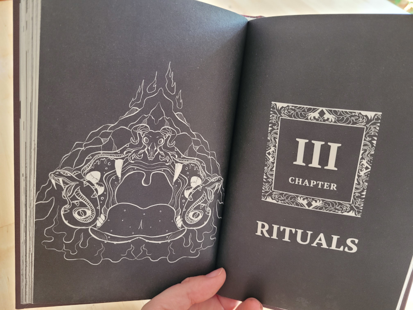 Zwei schwarze Buchseiten, links eine düstere Zeichnung, rechts eine römische Drei und die Worte Chapter und Rituals