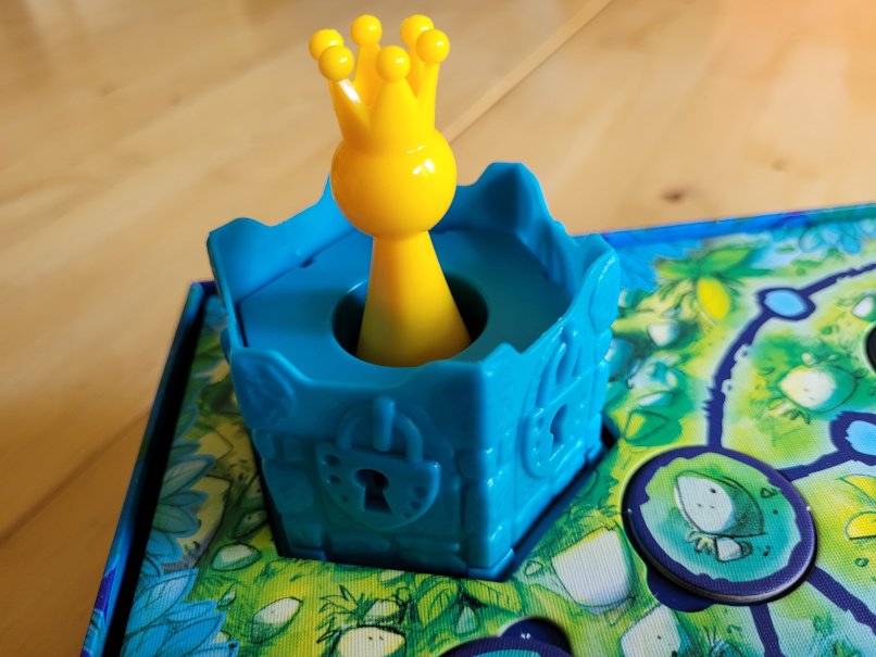 Eine gelbe Spielfigur mit Krone sitzt in einem Turm auf dem Schlösser zu sehen sind.
