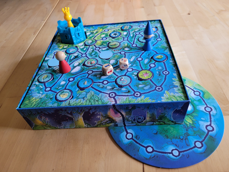 Der Spielaufbau von "Der verzaubete Turm" mit Figuren, Würfeln, Spielschachtel, die zugleich Spielplan ist und dem Turm mit der Prinzessin.