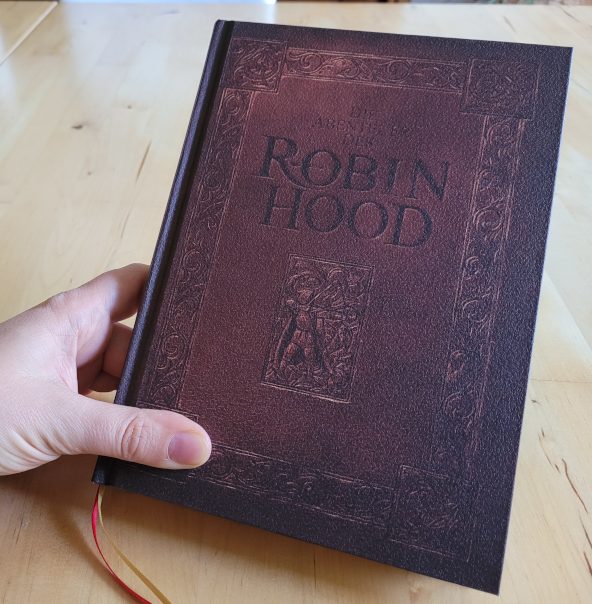 Eine Hand hält ein Buch mit der Aufschrift "Die Abenteuer des Robin Hood".