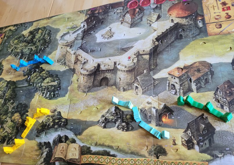 Der Spielplan zeigt eine Burg, einen Wlad und ein Dorf. Auf den Wegen stehen Spielfiguren.