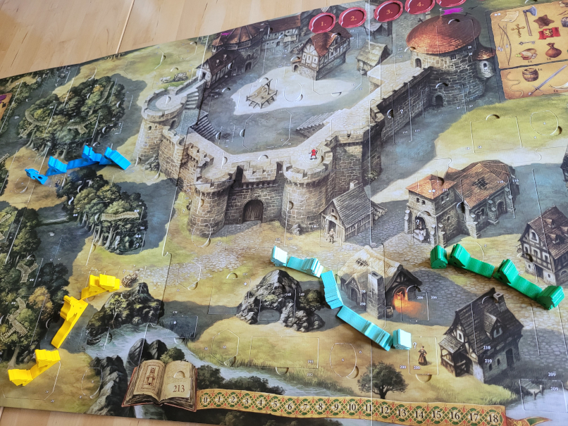 Der Spielplan zeigt eine Burg, einen Wlad und ein Dorf. Auf den Wegen stehen Spielfiguren.