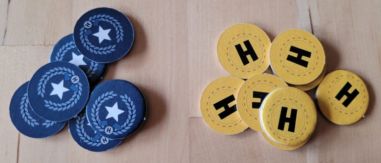 Sechs blaue und acht gelbe, runde Chips aus Karton. Auf den blauen Chips ist ein Stern zu sehen, auf den gelben ein "H".