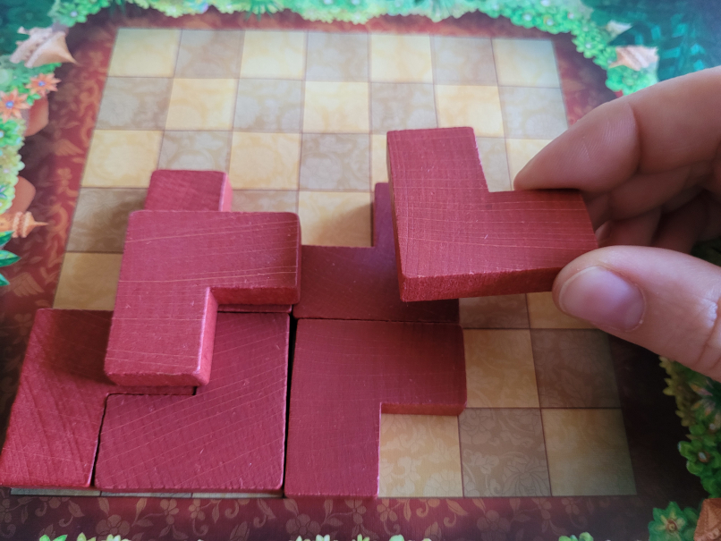 Eine Hand hält einen Spielstein über den Spielplan mit einigen anderen Bausteinen von "Plateau X".
