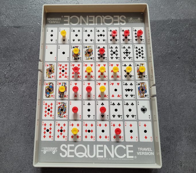 Das Spielplan von "Sequence Travel" mit Spielkarten und gelben und roten Markern.