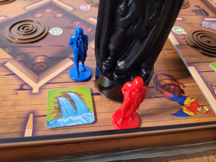 Zwei Matrosen stehen neben dem Captain-Figur und einem Leck-Plättchen an Deck.
