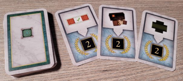 Ein Stapel verdeckte Brunnenkarten aus "Carpe Diem" und drei aufgedeckte Karten, die Siegpunkte bringen.