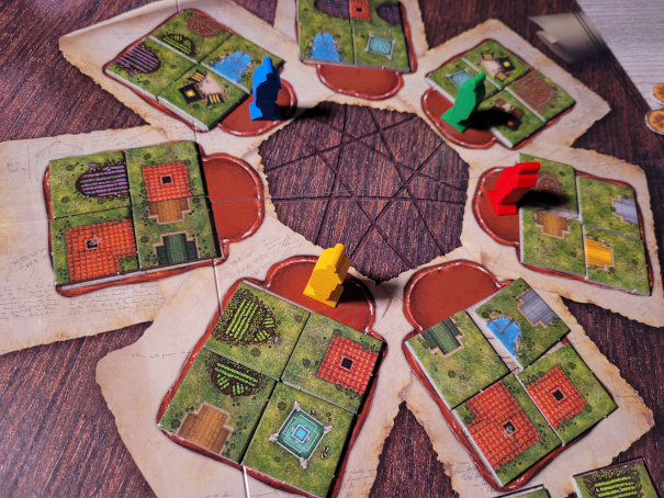 Der Spielplan von "Carpe Diem" mit je vier Plättchen, die im Kreis angeordnet sind. Dazwischen stehen vier Spielfiguren.