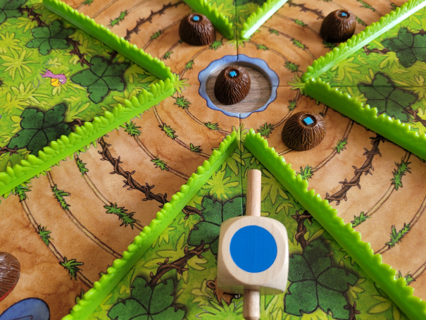 Der Kreisel zeigt die blaue Seite. Auf dem Spielplan sind drei blaue Kokosnüsse unterschiedlich nah am Teich, eine liegt im Teich.