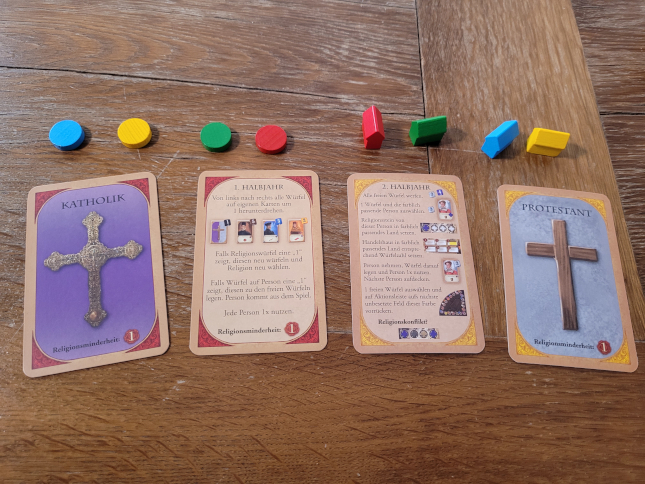 Vier Karten mit Religionen und Spielübersichten, darüber in einer Reihe Holzplättchen und Holzhäuschen in Spielerfarben.