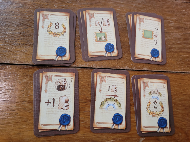 Sechs Stapel Karten mit verschiedenen Symbolen und einem aufgedruckten blauen Wachssiegel.