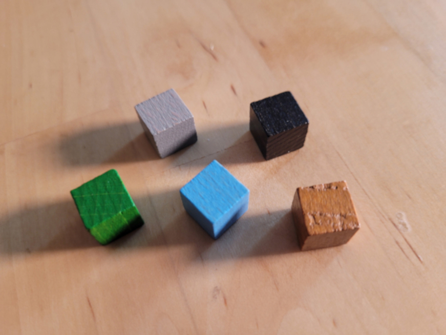 Fünf Würfel in Blau, Braun, Grün, Grau und Schwarz.