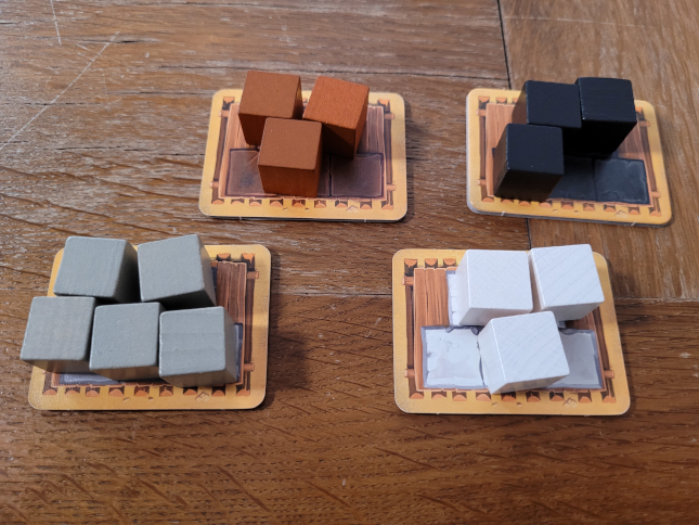 Auf vier Kartonplättchen liegen sortierte Holzwürfel in Braun, Schwarz, Grau und Weiß.