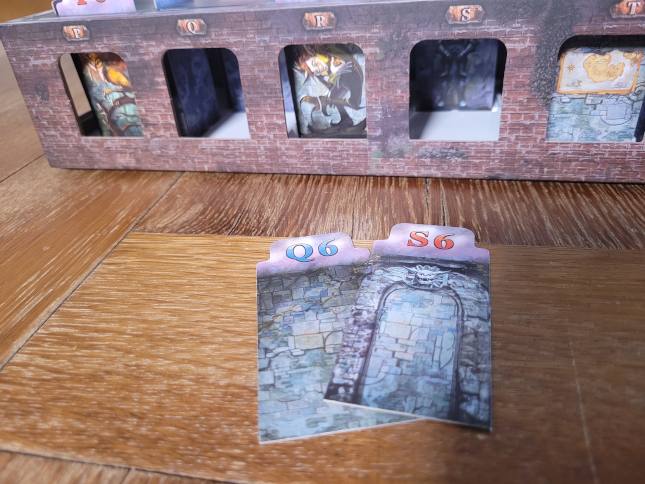 Zwei Wandkarten sind aus dem Raster gezogen und liegen neben der Spielschachtel.