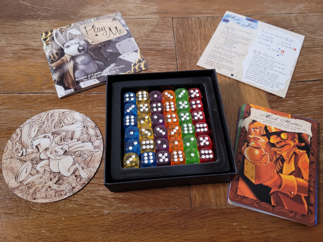 Das Spielmaterial von "Play Me – Alice in Wonderdice" mit vielen Karten und Würfeln.