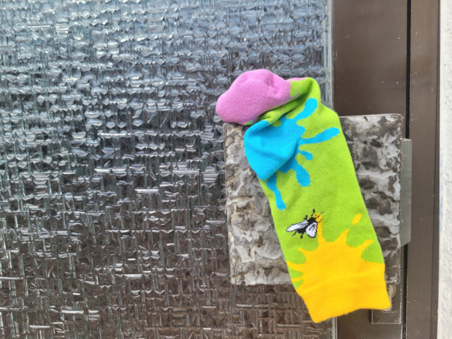 Die Socke mit den Farbklecksen hängt an einem Türknauf.