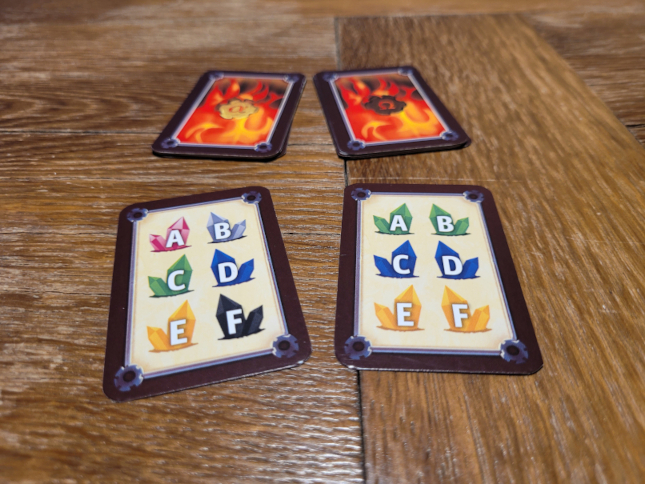 Vier Karten. Zwei mit Flammen auf der Rückseite, zwei mit sechs bunten Kristallen, jeweils mit den Buchstaben A bis F.