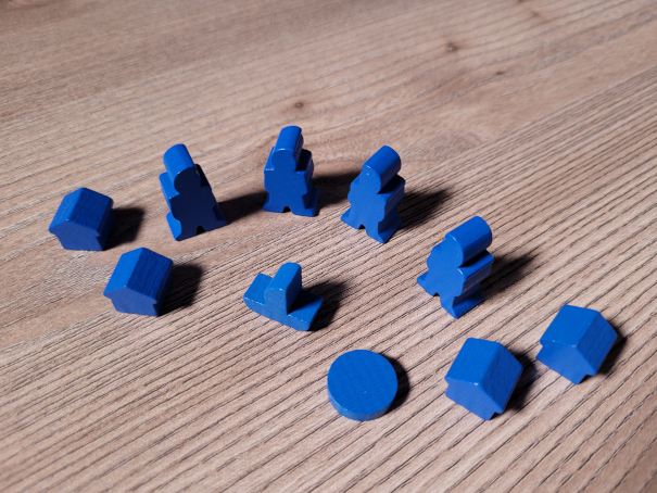 Das Spielmaterial aus Holz des blauen Spielers mit Spielfiguren, Häuschen, einem Boot und einer Scheibe.