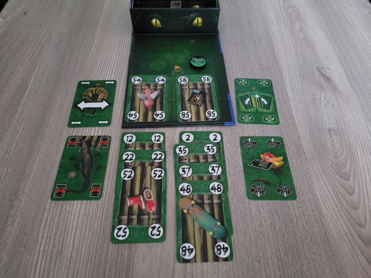Das Spielmaterial von "Allie Gator", viele Karten mit Zahlen, dazu ein Spielplan, auf dem der Allie-Marker liegt. Drumherum liegen die Sonderkarten mit verschiedenen Symbolen.