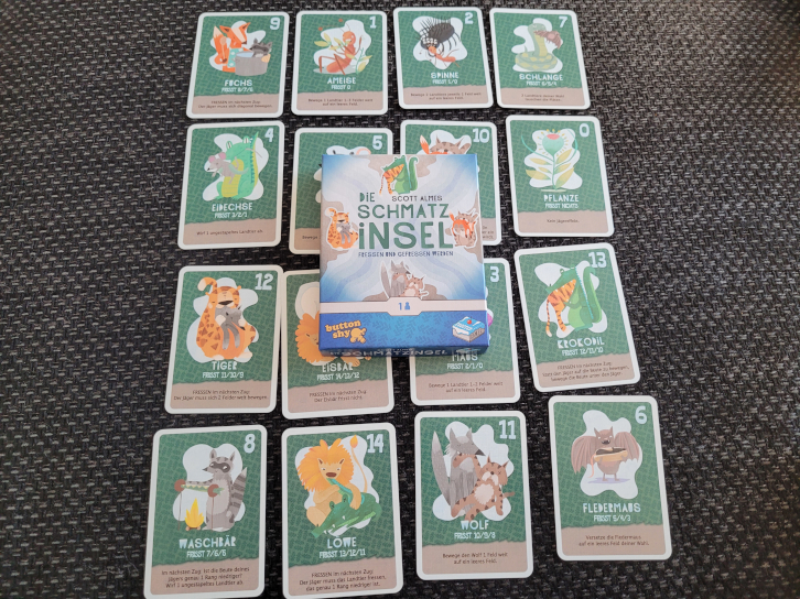 Ein Raster mit vier mal vier Karten mit den Zahlen Null bis Sechzehn und verschiedenen Tieren. In der Mitte liegt die Schachtel von "Die Schmatzinsel".