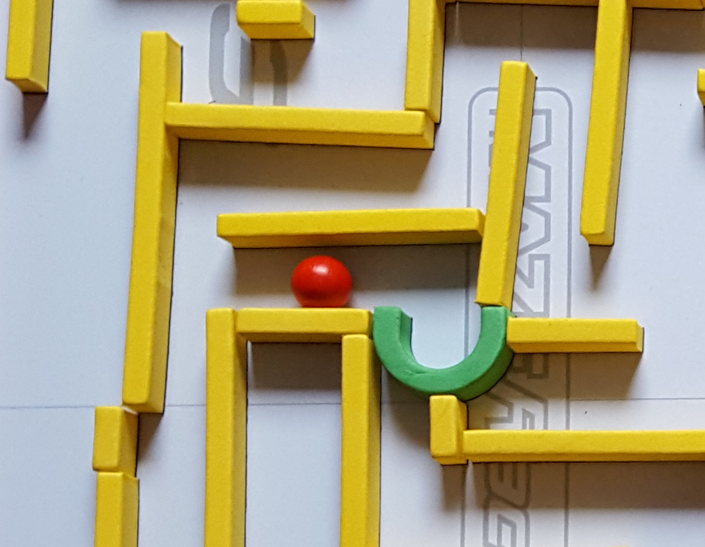 Ein grüner Bogen und eine rote Kugel liegen zwischen gelben Labyrinthwänden.