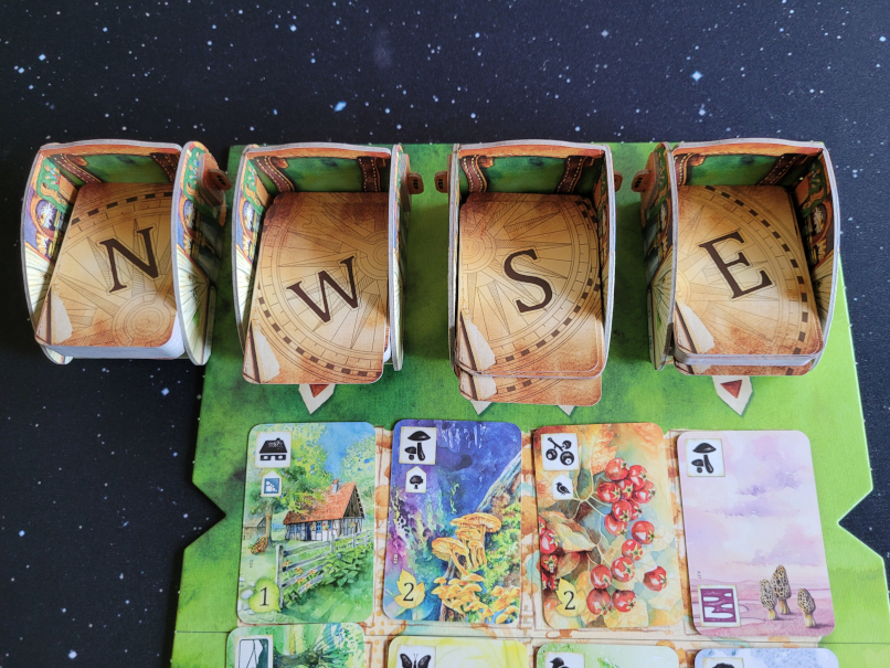 Vier Karren aus Karton, darin die Kartenstapel mit den Buchstaben N, W, S und E auf der Rückseite.