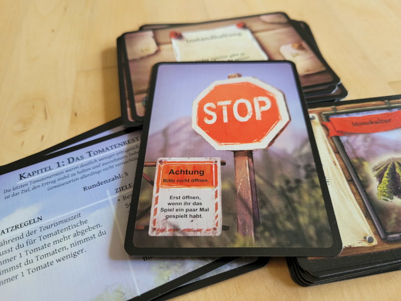 Auf mehreren Kartenstapeln liegt eine Karte mit einem Stop-Schild und der Aufschrift "Erst öffnen, wenn ihr das Spiel ein paar mal gespielt habt."