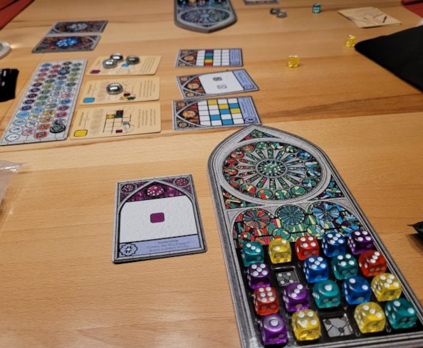Auf einem Tisch ist das Spielmaterial von Sagrada aufgebaut mit Würfeln und Karten.