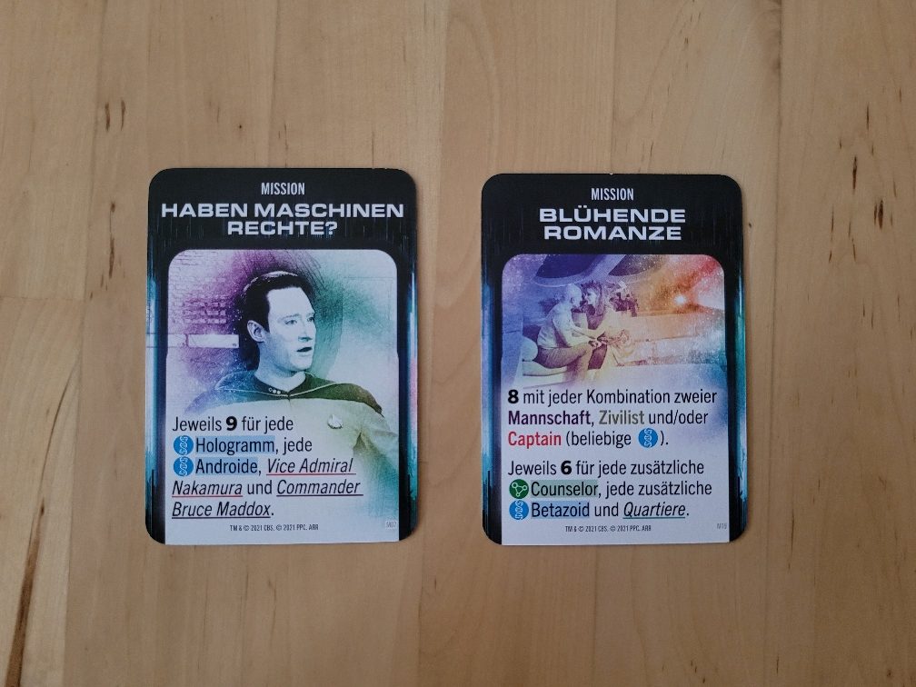 Zwei Missionskarten mit den Titeln "Haben Maschinen Rechte?" und "Blühende Romanze" sowie mit Bildern, Text und Symbolen.