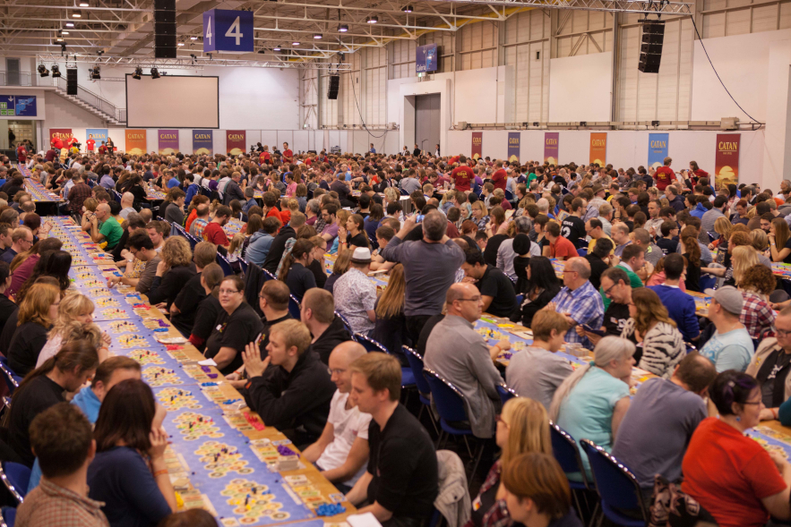 In einer großen Halle sitzen an langen Tischreihen Menschenmassen und spielen "Catan".