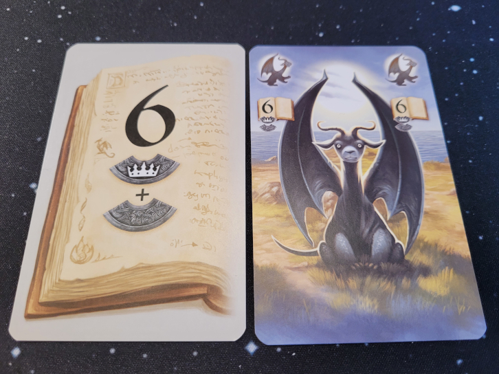 Eine Karte mit einer Buchseite, der Zahl sechs und zwei Amulettsymbolen. Eine Karte mit einem schwarzen Drachen, hinter dem die Sonne leuchtet.