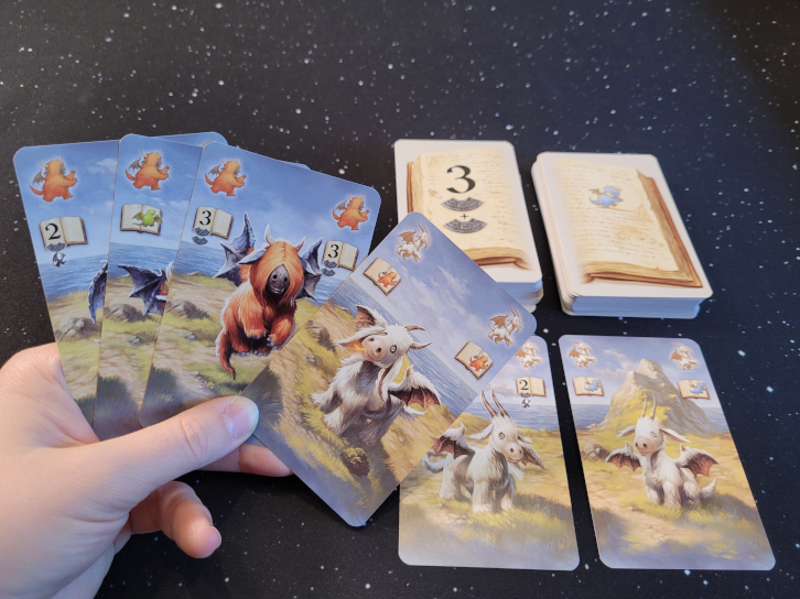 Eine Hand hält vier Karten über zwei Kartenstapel und zwei ausliegende Karten.