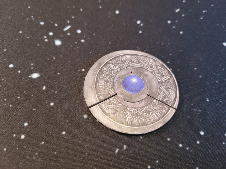 Drei Amulett-Stücke sind zu einem Kreis zusammengelegt. In der Mitte liegt eine blaue Perle