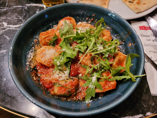 Ein Teller mit Tortellini in Tomatensoße mit viel Parmesan und frischem Rucola.