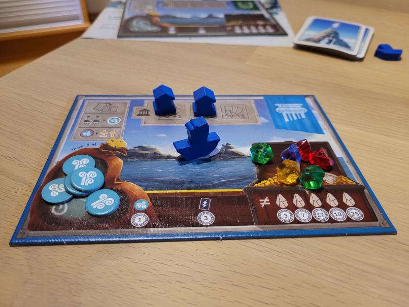 Ein Spielertableau mit Windplättchen, bunten Kristallen und drei Spielfiguren: einem Boot und zwei Tempel.