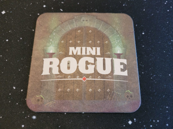 Ein Bierdeckel mit der Aufschrift "Mini Rogue", im Hintergrund ein altes, beschlagenes Tor.