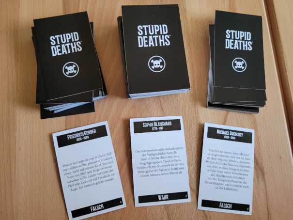 Drei Stapel Quizkarten aus "Stupid Deaths. Davor liegt jeweils eine aufgedeckte Karte.