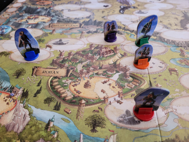Auf einem Spielplan ist die Stadt Rohan zu sehen. Darumherum fünf Spielfiguren.