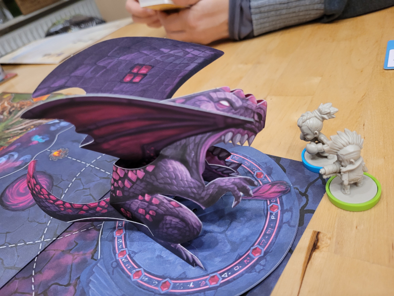 Ein lilafarbener Pop-up-Drache und zwei Spielfiguren.